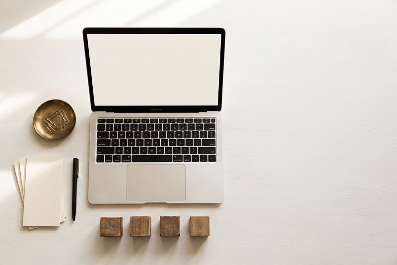 An open laptop, blank payment vouchers and a pen arranged on a warm white desk.
